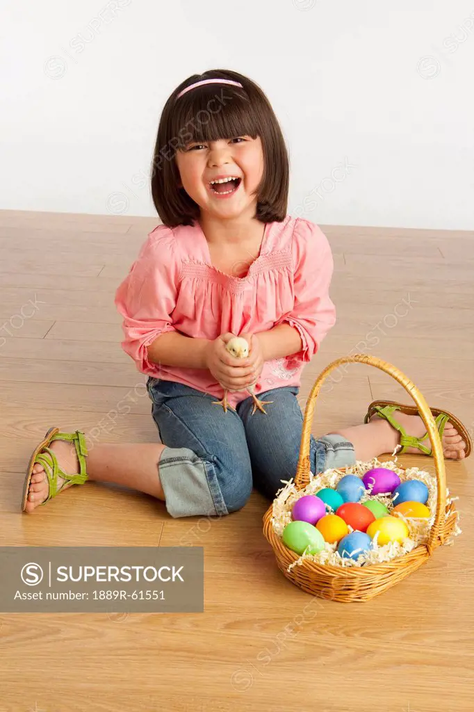 A Girl Holding A Chick And Sitting With A Basket Full Of Colorful Easter Eggs