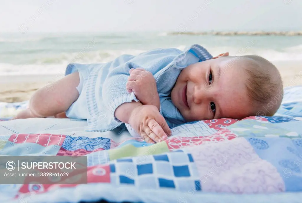 A Baby Boy Laying On A Blanket On The Beach, Benalmadena Costa, Costa Del Sol, Malaga, Andalusia, Spain
