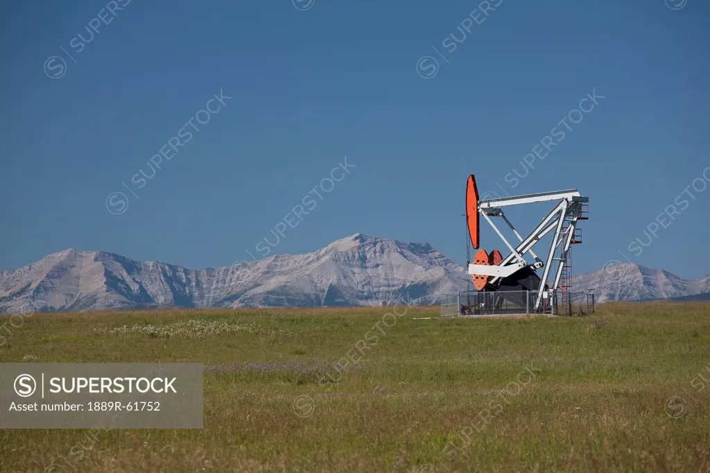 Pumpjack With Mountains And Blue Sky In The Background, Alberta, Canada