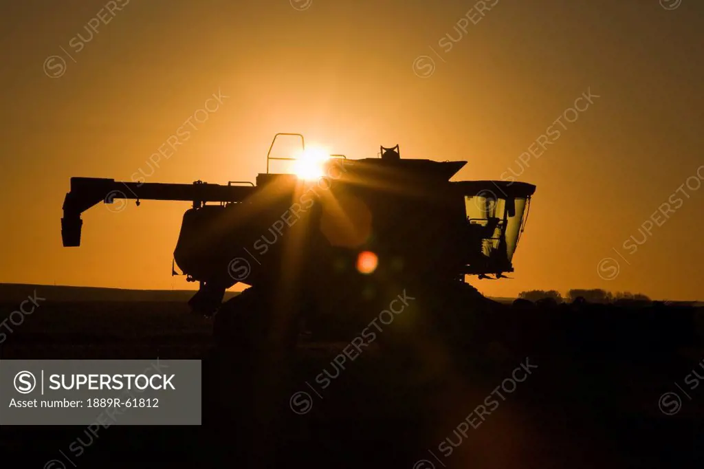 silhouette of a combine with a sunburst at sunrise, alberta, canada