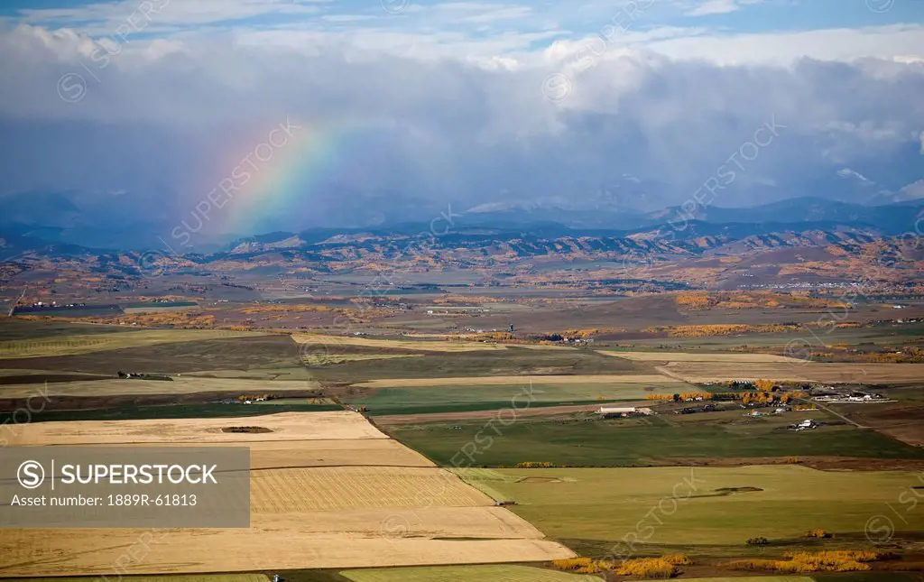 a rainbow over the mountains with storm clouds and the colors of autumn in fields, alberta, canada