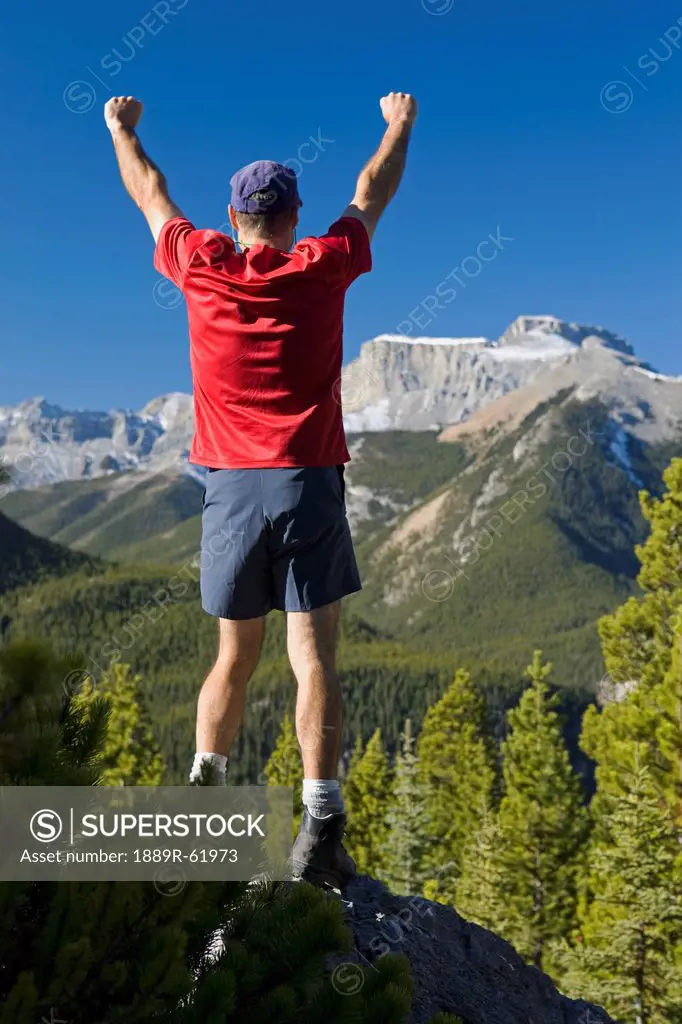 male hiker on top of a ridge overlooking a valley and mountain view, alberta, canada
