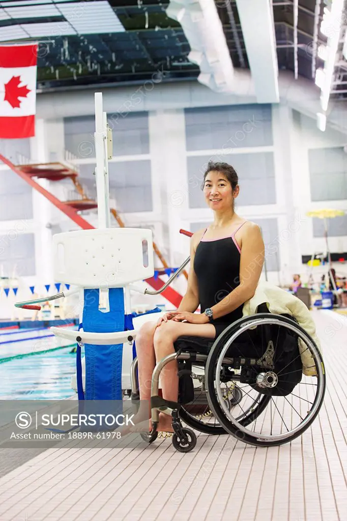 a woman in a wheelchair sits beside a lift on the edge of a swimming pool, edmonton, alberta, canada