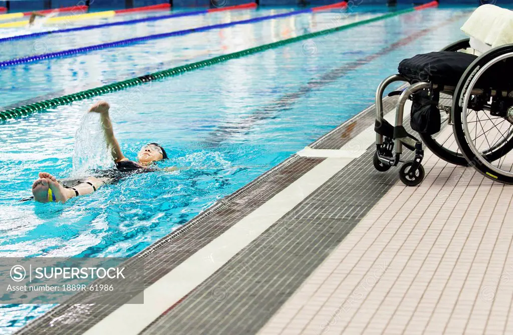 a paraplegic woman swims in a pool with her wheelchair at the edge of the pool, edmonton, alberta, canada