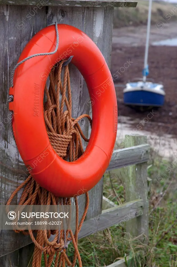 an orange life preserver ring and rope hanging on a wooden shed wall, northumberland, england