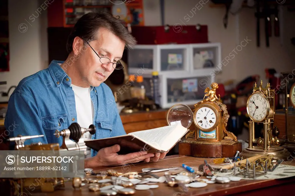 a clock maker and repairman taking time to read his bible in his shop, st. catharines, ontario, canada