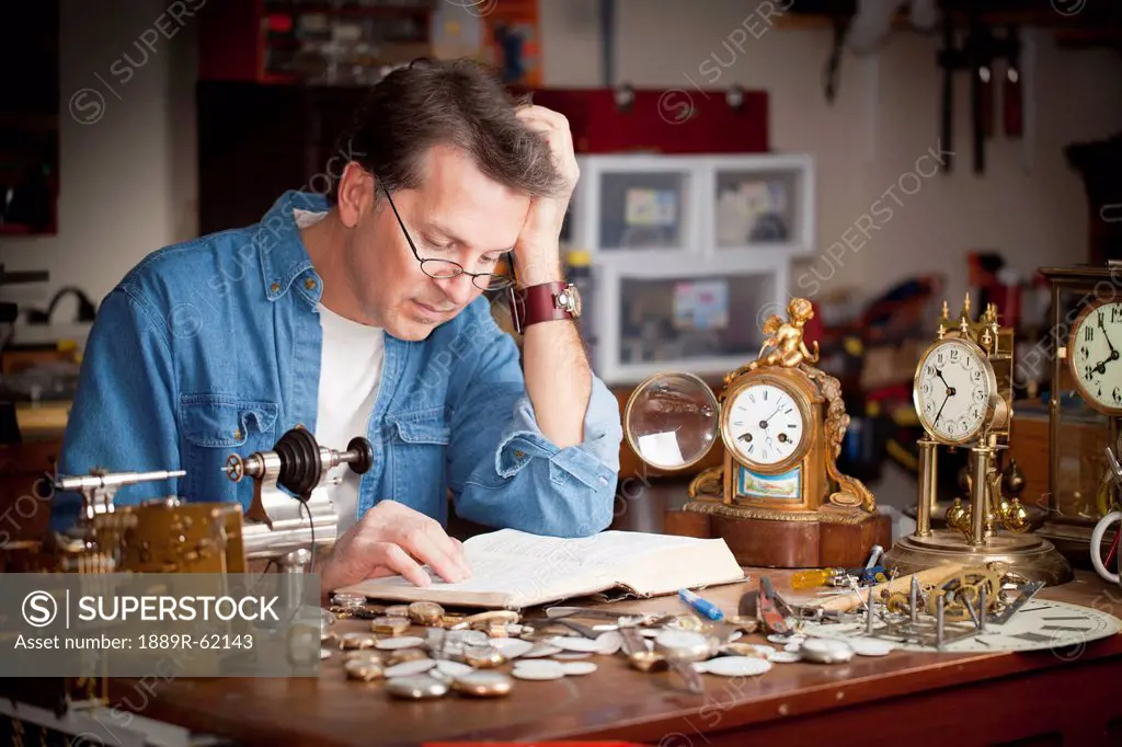 a clock maker and repairman reading his bible in his shop, st. catharines, ontario, canada