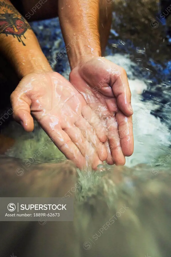 hands touch the cascade of water at currumbin rock pools in currumbin valley, gold coast, queensland, australia