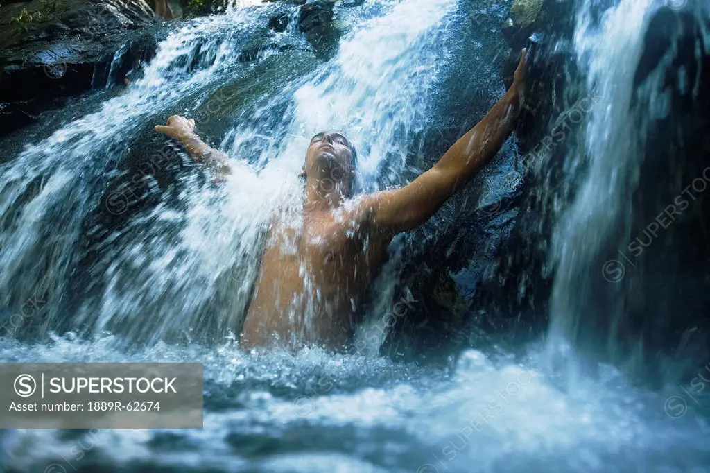 a man standing under a waterfall with arms outstretched at the currumbin rock pools in currumbin valley, gold coast, queensland, australia