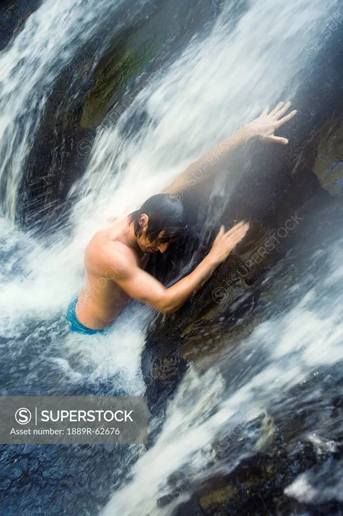 a man standing under a waterfall at the currumbin rock pools in currumbin valley, gold coast, queensland, australia