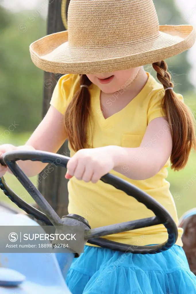 a girl with a straw hat with hands on the steering wheel of a tractor, troutdale, oregon, united states of america