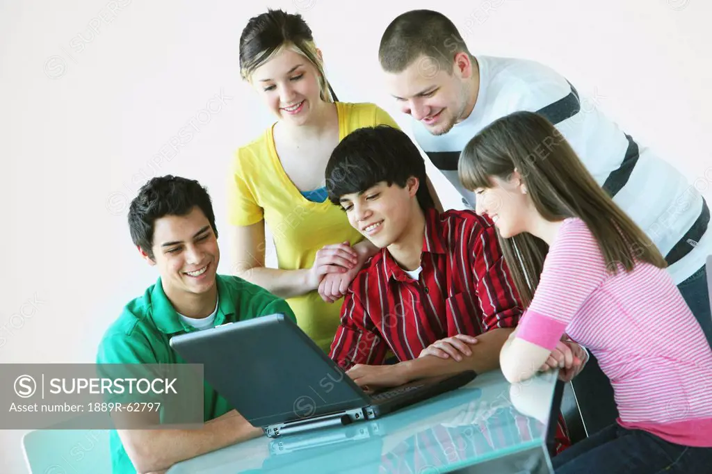 a group of teenagers gathered around a laptop computer
