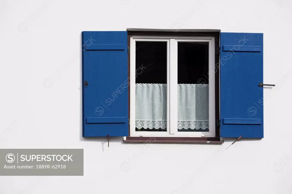bright blue shutters on a white wall with lace curtains in the window, oberstdorf, germany