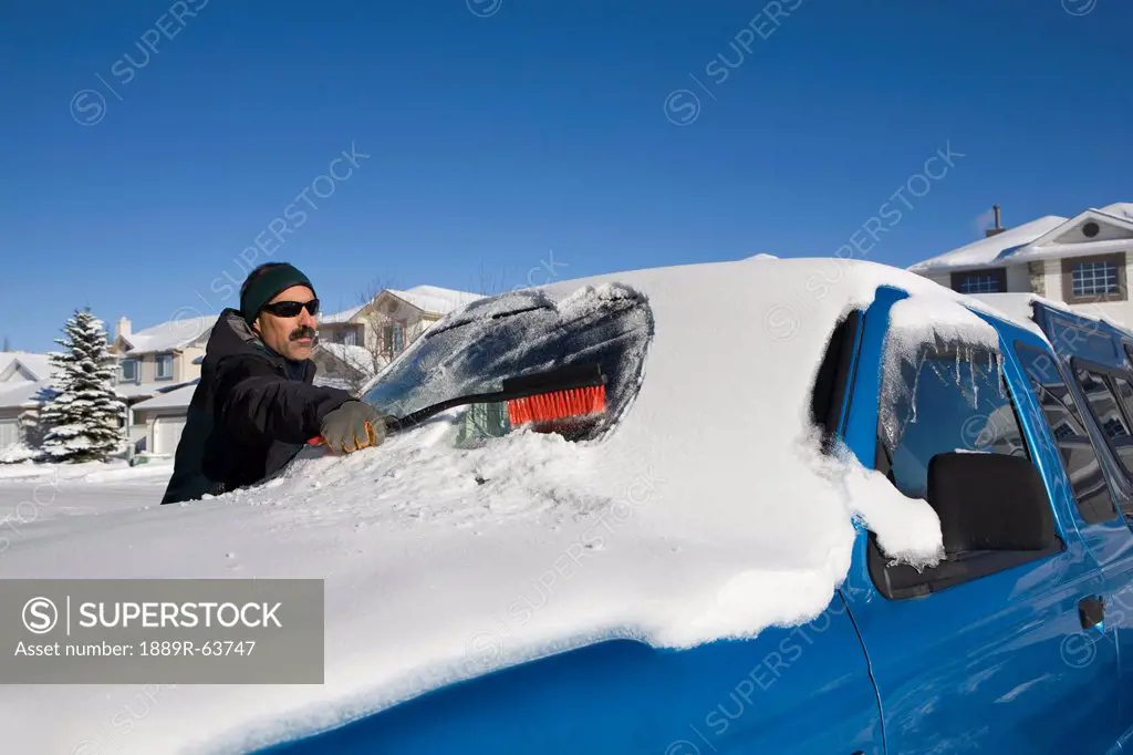 man brushing snow off a vehicle´s windshield, calgary, alberta, canada