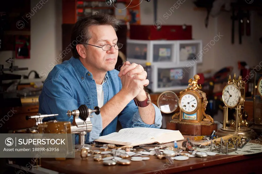 a clock maker prays at his desk in his shop, st. catharines, ontario, canada