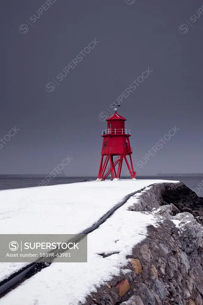 a red lighthouse under a stormy sky along the coast in winter, south shields, tyne and wear, england