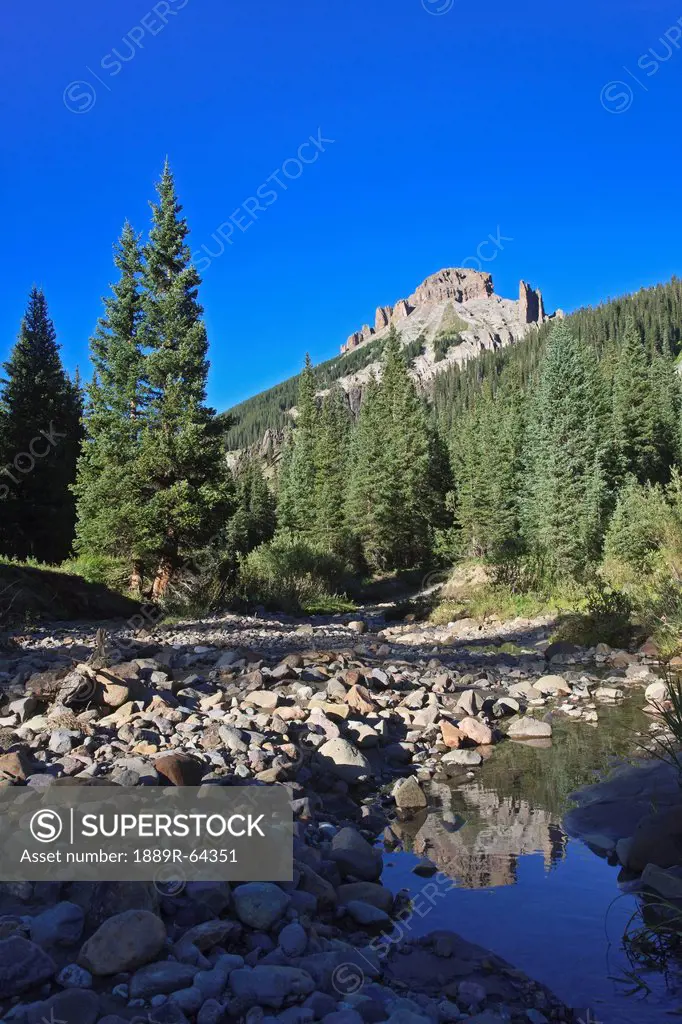 rugged mountain peak reflected in a stream with a conifer forest in the san juan mountains, colorado, united states of america