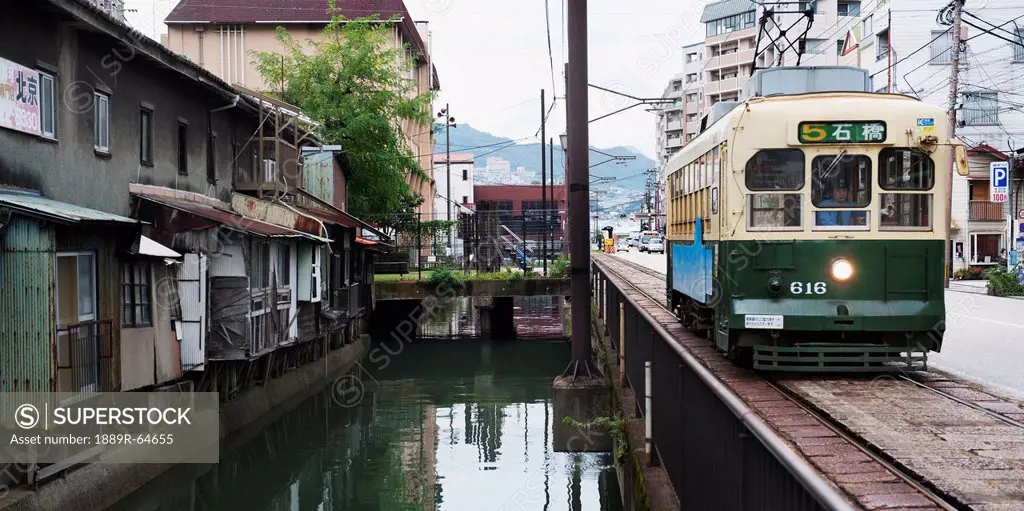 a train travels beside housing and a canal, nagasaki, japan