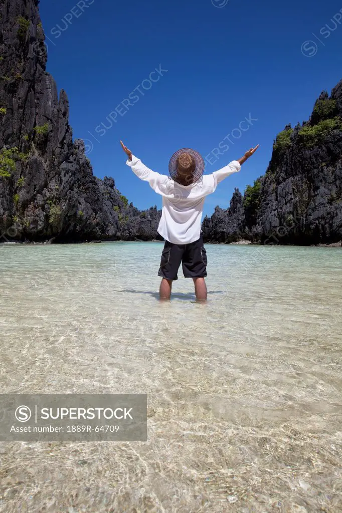a man enjoys the sunshine and scenery in a small lagoon on miniloc island, near el nido, miniloc island, el nido, bacuit archipelago, palawan, philipp...
