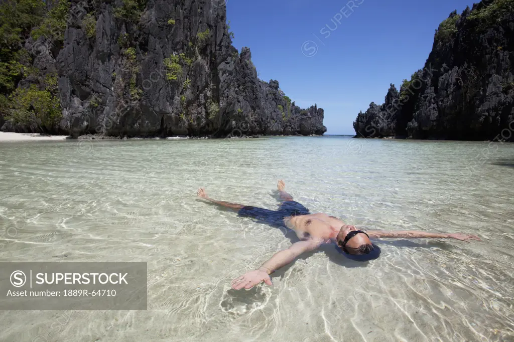 man floating on his back in a lagoon, miniloc island, palawan, philippines