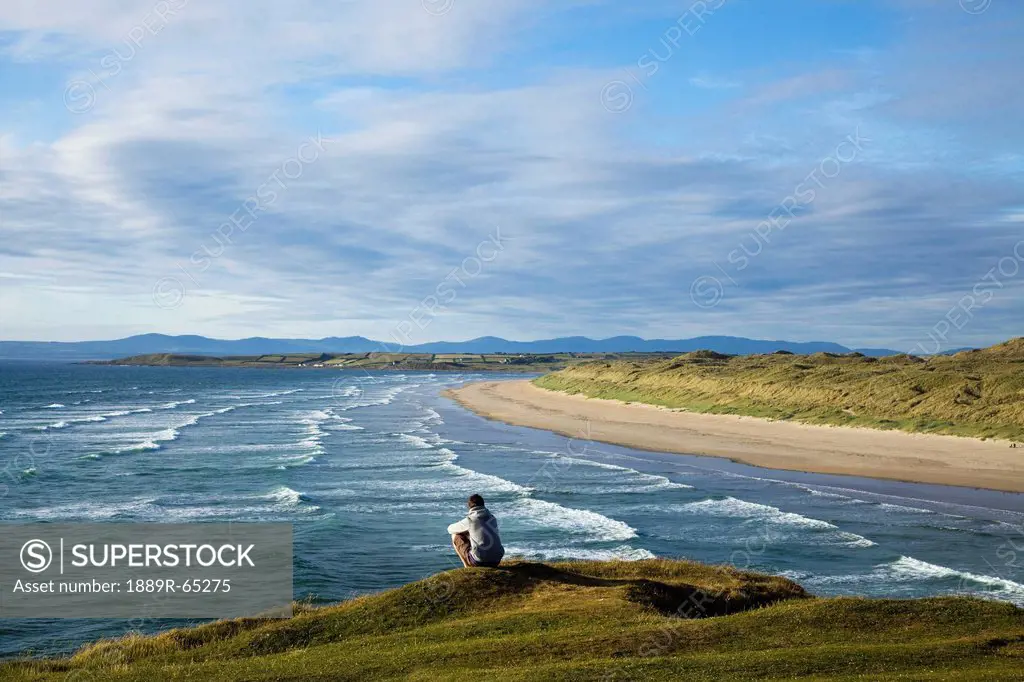 A Person Sitting At The Water´S Edge At The Beach Near Bundora, County Donegal, Ireland