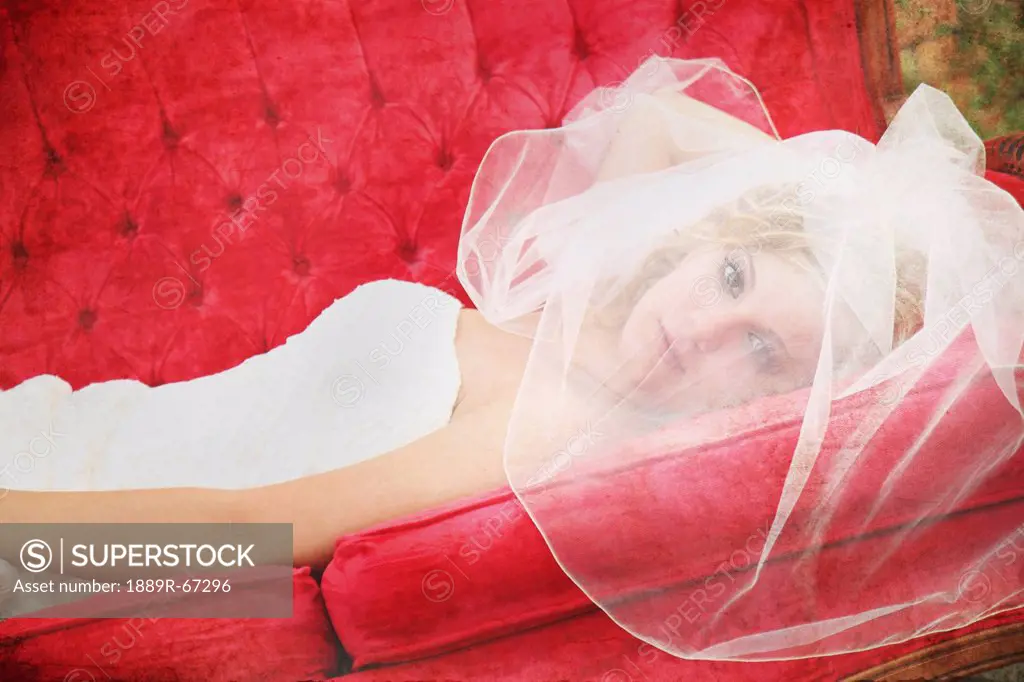 a bride´s face behind her veil as she lays on a red couch