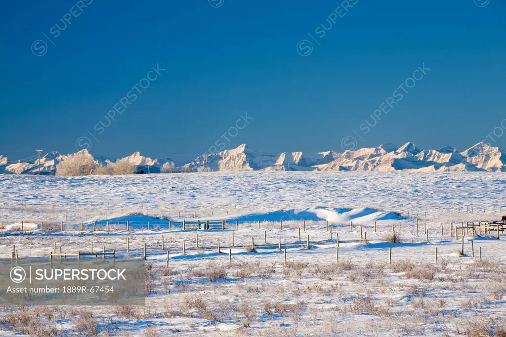 fencing and snowy field against canadian rockies, cochrane, alberta, canada