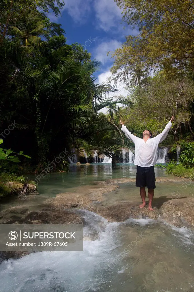 a man raises his arms in praise at tranquil waterfall, cambugahay falls, siquijor, philippines
