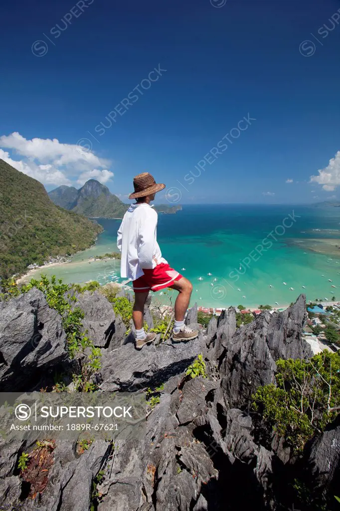 man enjoys view from limestone spires over coastal village, el nido, palawan, philippines
