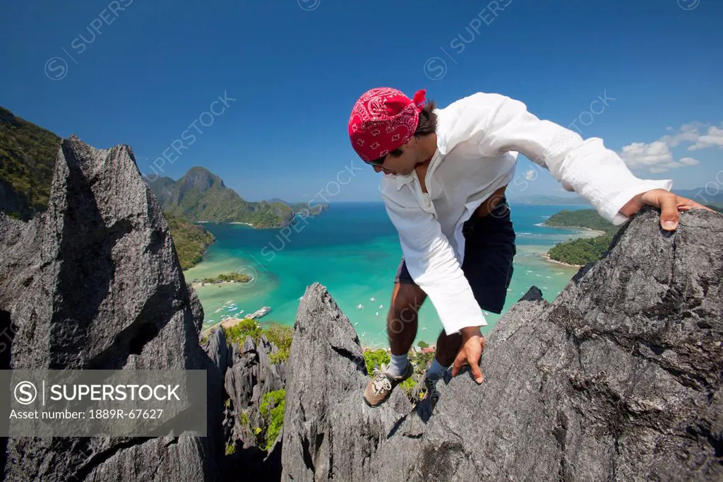 a man rock climbs on top of sharp limestone spires overlooking the village of el nido, el nido, bacuit archipelago, palawan, philippines
