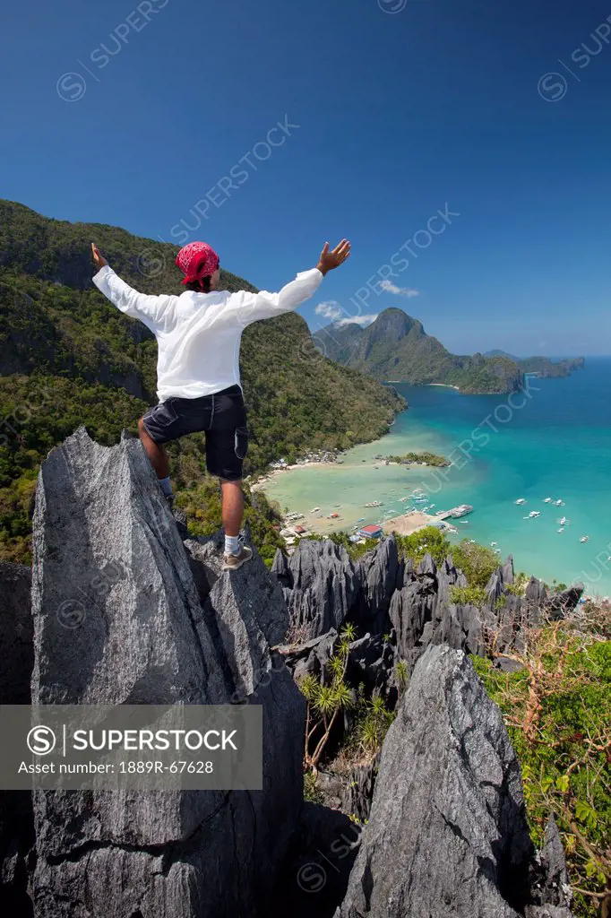 a man raises his arms in praise on top of sharp limestone spires overlooking the village of el nido, el nido, bacuit archipelago, palawan, philippines