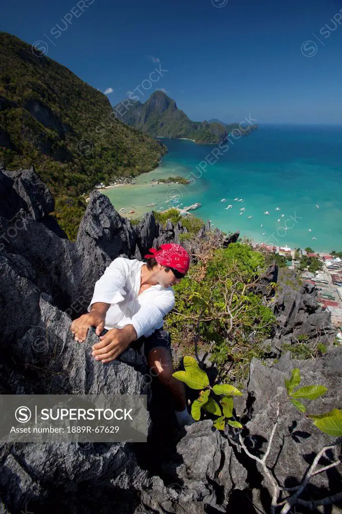 a man rock climbs on top of sharp limestone spires overlooking the village of el nido, el nido, bacuit archipelago, palawan, philippines