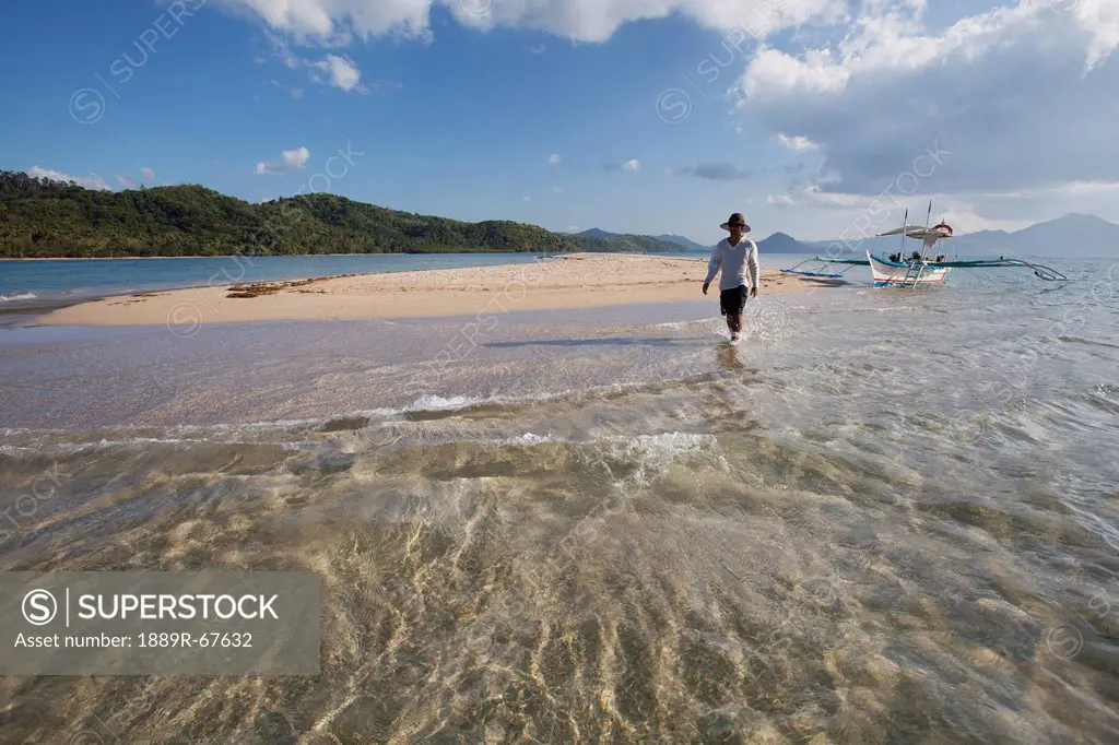 a male tourist walks along the white sand on a small island near el nido, bacuit archipelago, palawan, philippines