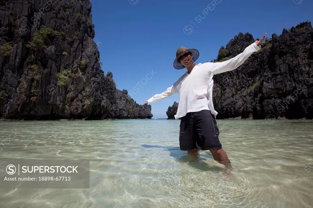 man standing in clear water of small lagoon, miniloc island, palawan, philippines