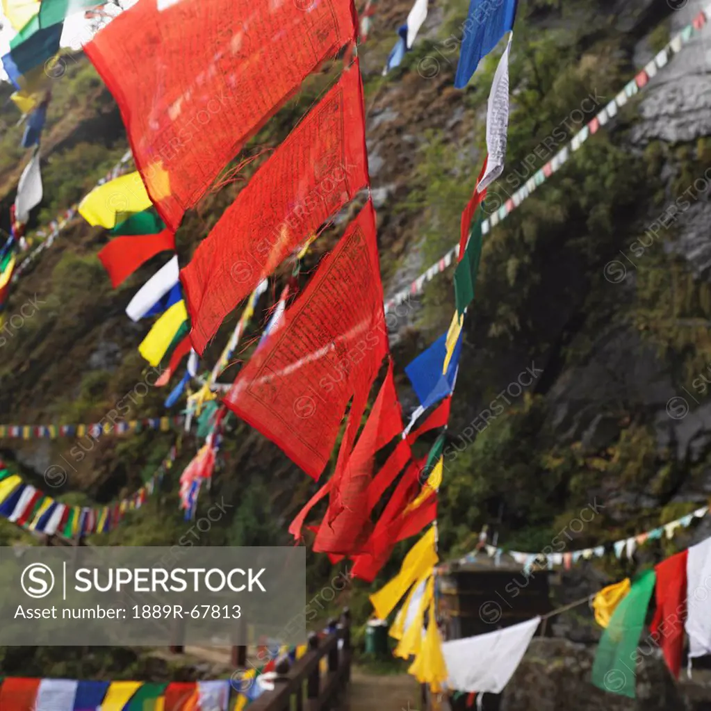 prayer flags hanging over a wooden walkway at tiger´s nest monastery, paro valley, taktsang, bhutan