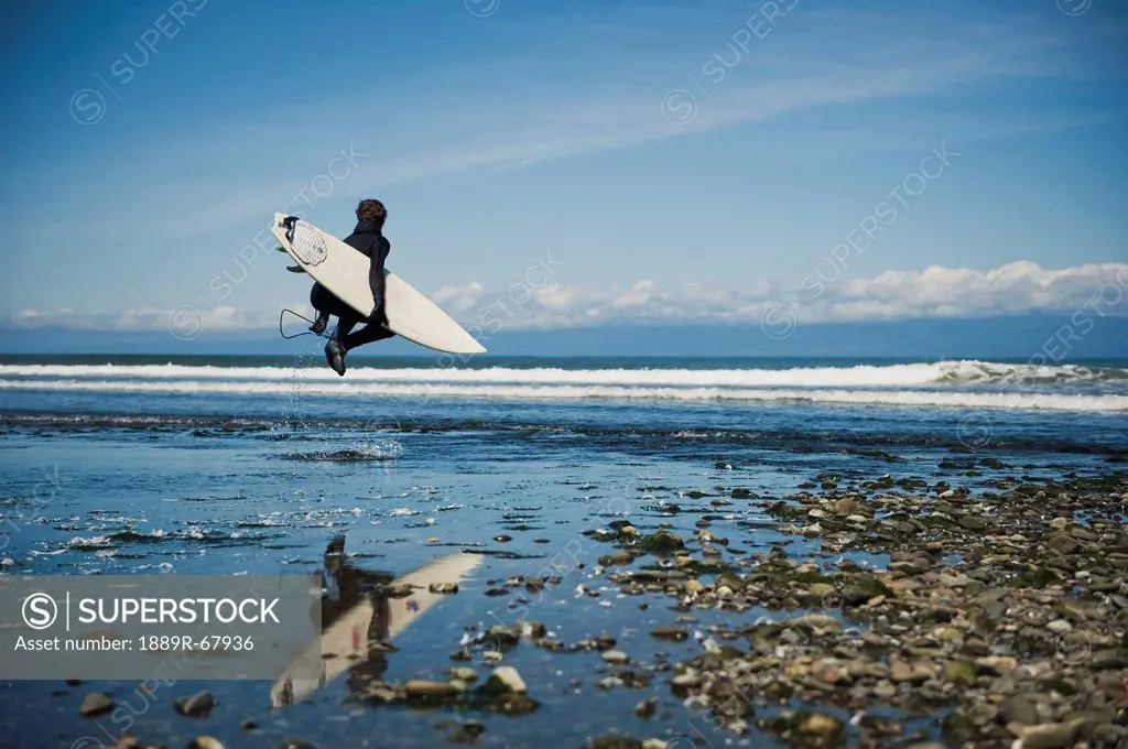 a man walks with his surfboard down the beach, washington peninsula washington united states of america