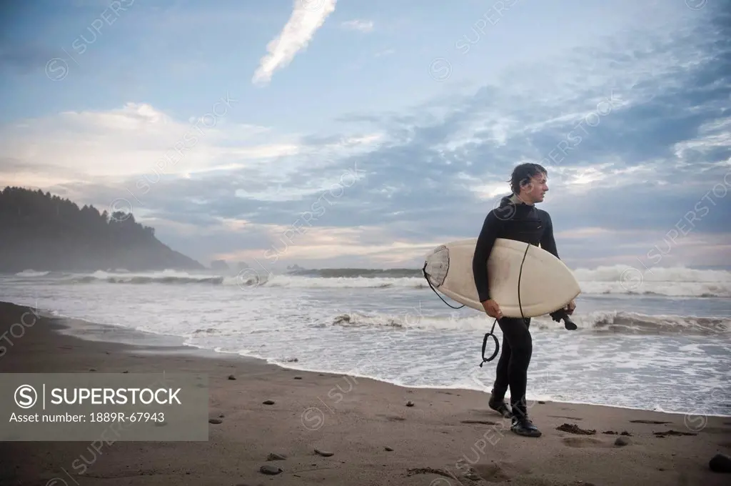 a young man carries his surfboard down the beach, la push washington united states of america