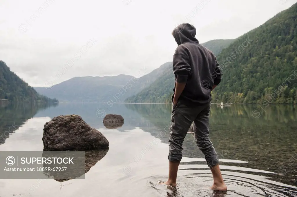 a young man wades in shallow water on cameron lake, british columbia canada