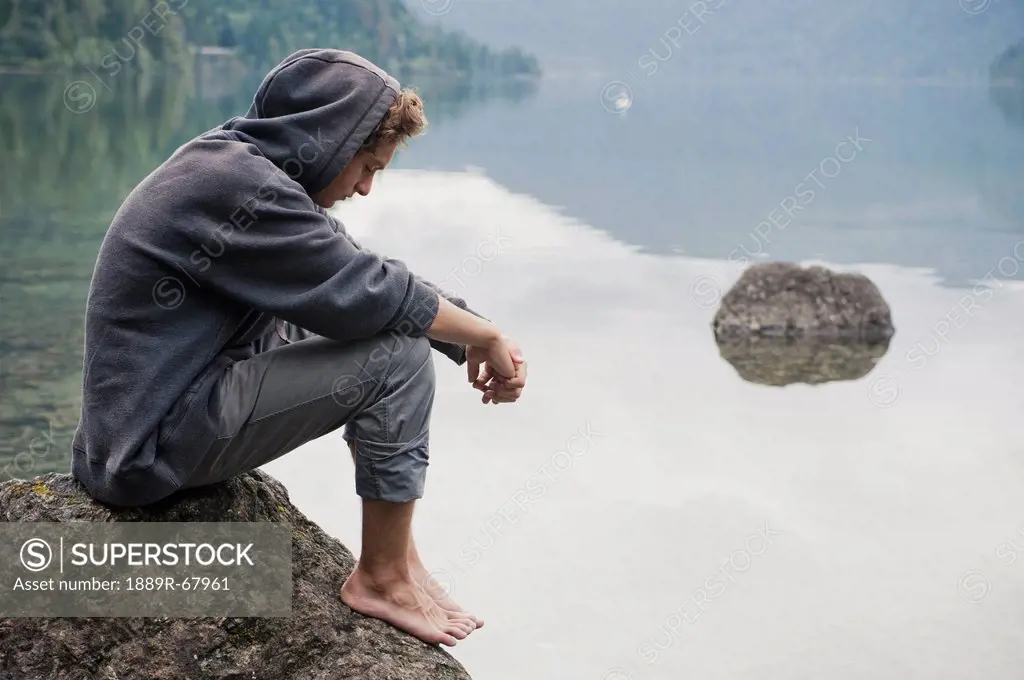 a young man sits on a rock in cameron lake, british columbia canada