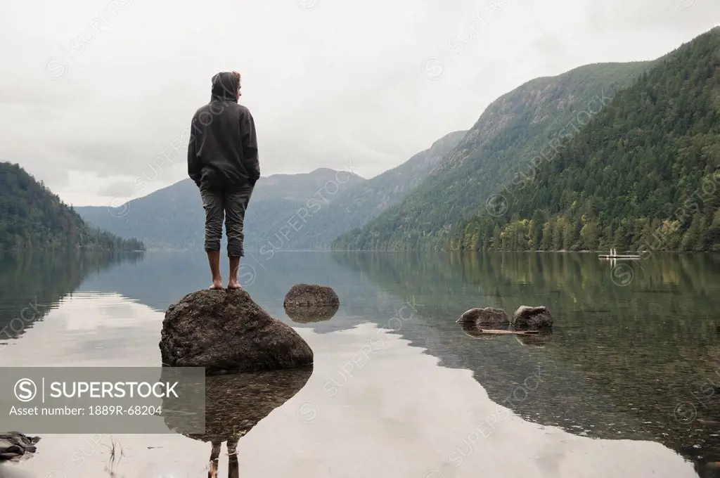 a young man stands on a rock looking out over cameron lake, british columbia canada
