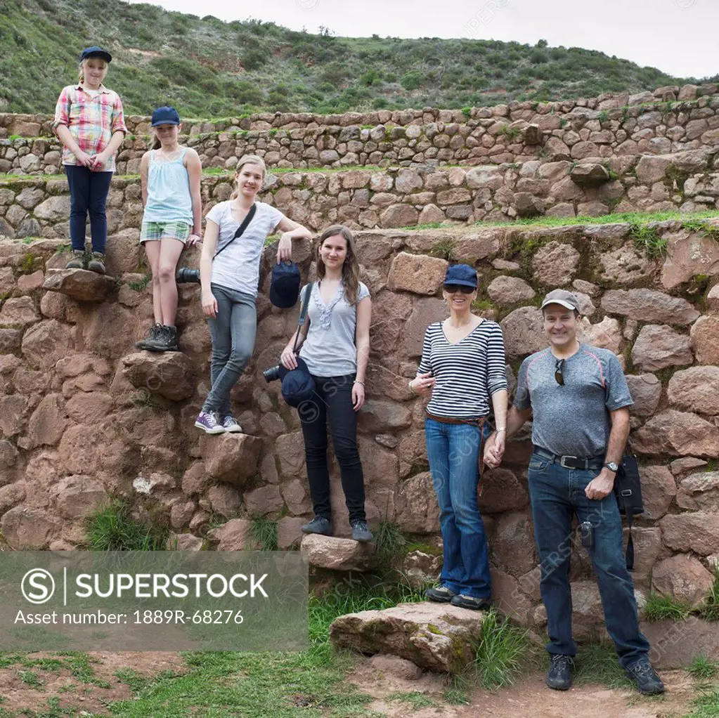 a family stands posing on rocks at the incan ruins, moray peru