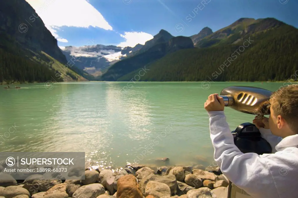 a boy looking through binoculars at a view of the mountains over lake louise, alberta canada