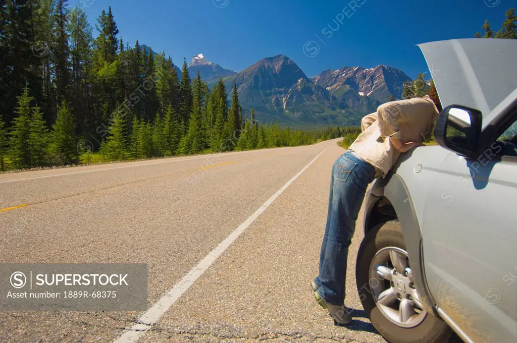 woman looking under hood of her car on mountain road, alberta canada