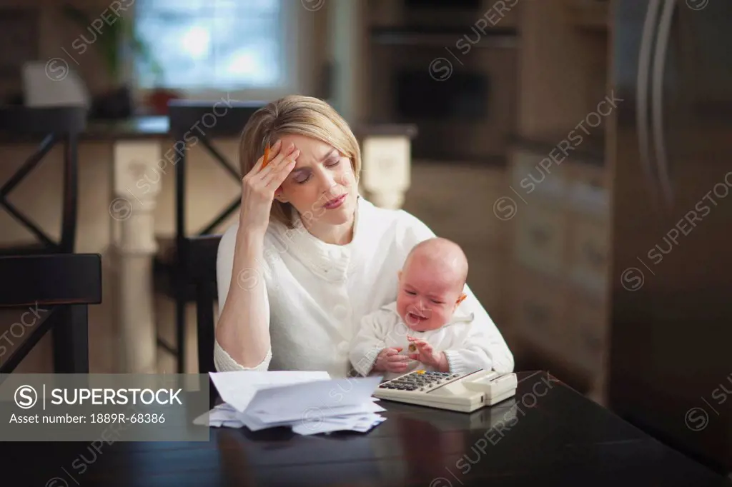 a mother holding a crying baby while stressed about bills and finances, jordan ontario canada