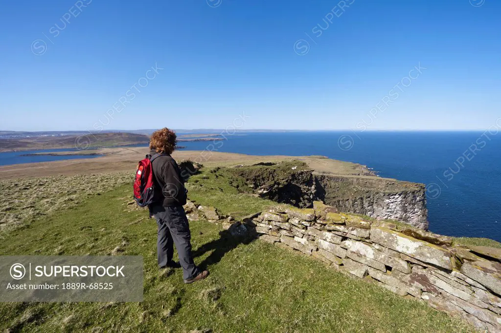 a woman stands looking out over the ocean, noss scotland