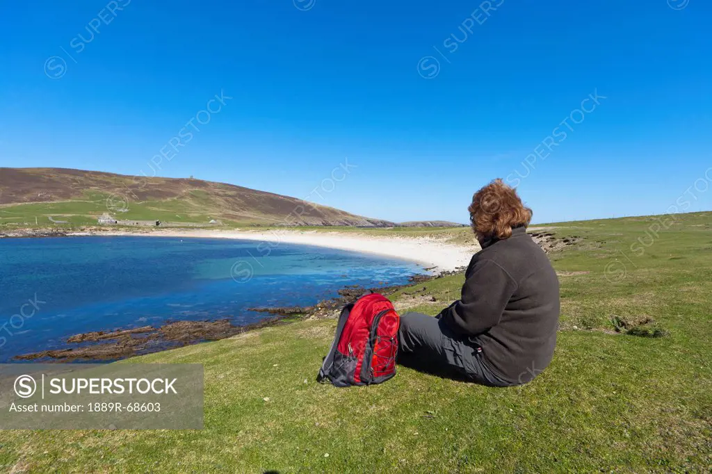 a woman sits with her backpack looking out over the coastline, noss scotland