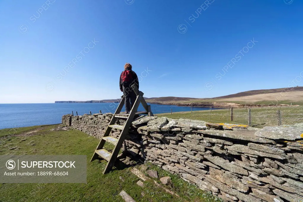 a woman by a stone wall along the coast, noss scotland