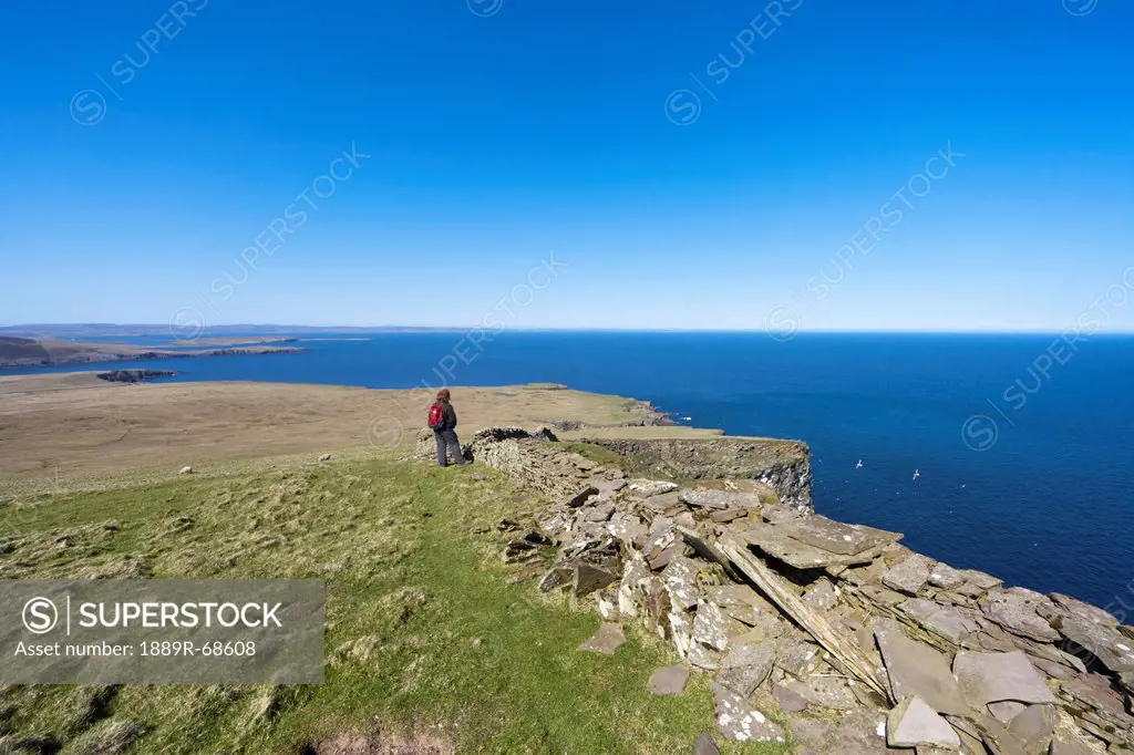 a woman standing along a ledge at the coast, noss scotland