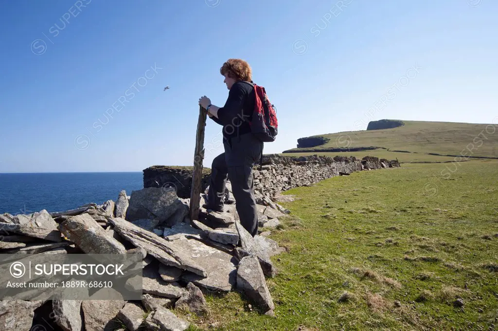a woman standing along a ledge at the coast, noss scotland
