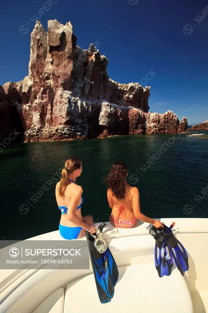 two tourists holding snorkeling gear as they sit on the edge of a boat at los islotes national marine park espiritu santo island, la paz baja californ...